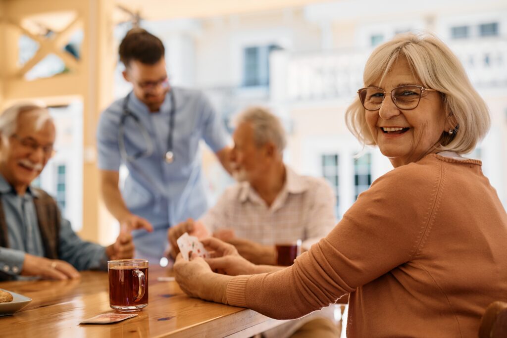 Happy mature woman enjoying in playing card with her friends on patio at residential care home.